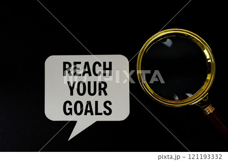 Reach Your Goals text on speech bubble with magnifying glass top view on black background 121193332