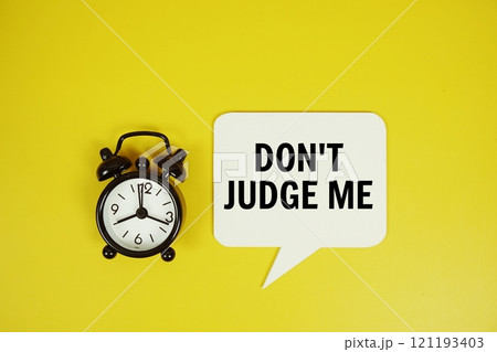 Don't judge me text on speech bubble with alarm clock top view on yellow background Don't judge me text on speech bubble with alarm clock top view on yellow background 121193403