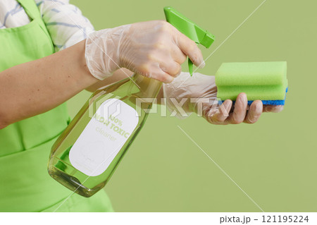 Modern woman in green apron and rubber gloves isolated on green Modern woman in green apron and rubber gloves isolated on green 121195224