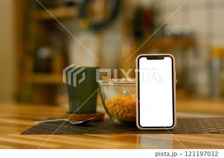 Smartphone with white screen near a bowl of cornflakes on kitchen table Smartphone with white screen near a bowl of cornflakes on kitchen table 121197012