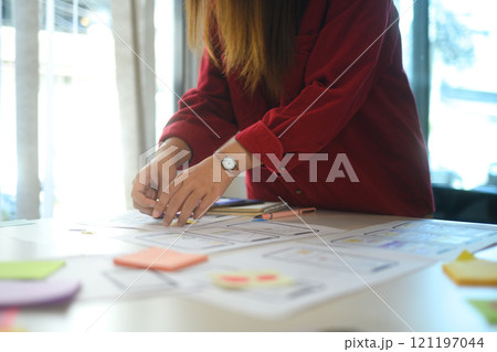 Close up of female designer arranging wireframe designs on desk covered with sketches and sticky notes Close up of female designer arranging wireframe designs on desk covered with sketches and sticky notes 121197044