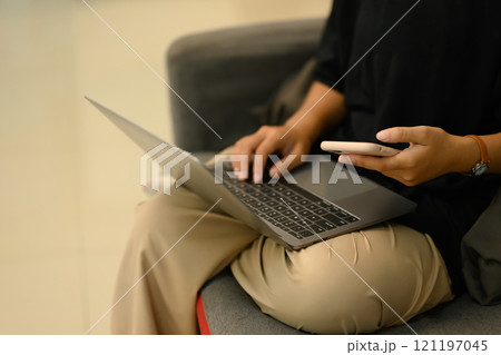 Cropped shot young woman working on laptop and using mobile phone at home 121197045