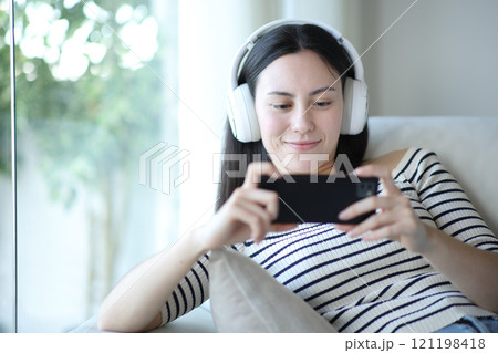 Asian woman watching media on phone wearing headphone Asian woman watching media on phone wearing headphone 121198418
