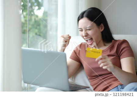 Excited asian woman buying online with laptop and card Excited asian woman buying online with laptop and card 121198421