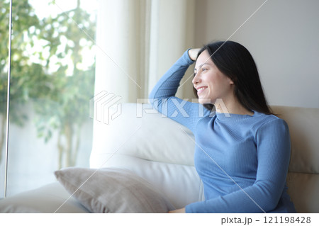 Happy asian woman relaxing looking through a window at home 121198428