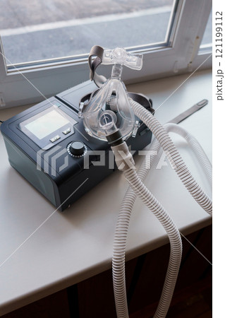 Medical CPAP Machine with Mask and Tubing on Windowsill 121199112