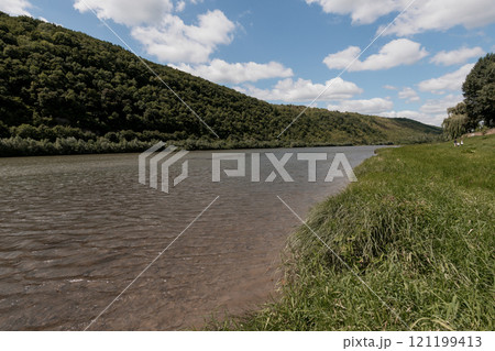 Serene Landscape of a River Bordered by Lush Green Hills Under a Cloudy Sky Serene Landscape of a River Bordered by Lush Green Hills Under a Cloudy Sky 121199413