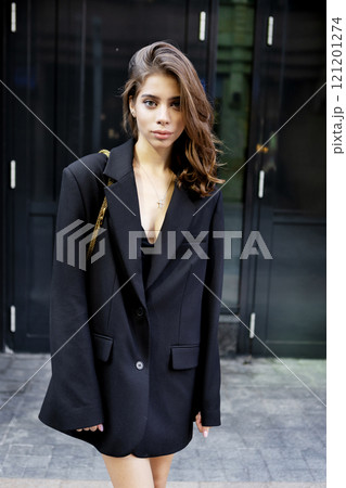 Portrait young woman wearing elegant outfit oversize black blazer, beautiful model stands, poses confidently in urban city. Modern high fashion, contemporary street style on minimalist backdrop Portrait young woman wearing elegant outfit oversize black blazer, beautiful model stands, poses confidently in urban city. Modern high fashion, contemporary street style on minimalist backdrop 121201274