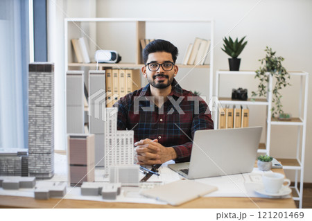 Young Indian male architect working in modern office with city model and laptop. Professional creating urban design plan. Young Indian male architect working in modern office with city model and laptop. Professional creating urban design plan. 121201469