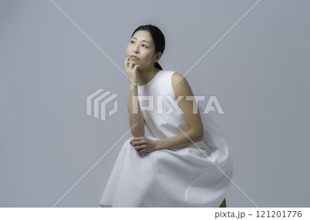 グレー背景の白いワンピースを着て椅子に座る若い女性のポートレート 121201776