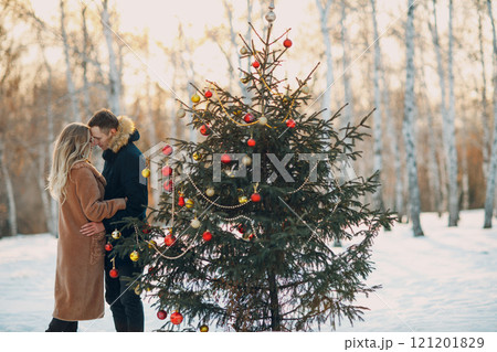 Young adult couple man and woman decorates pine tree in winter park forest. New year tree holiday party celebration concept 121201829