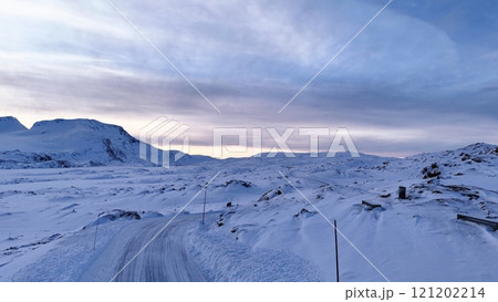 Snowy Mountain Landscape in Norway with Winding Road and Serene Winter Sky  121202214