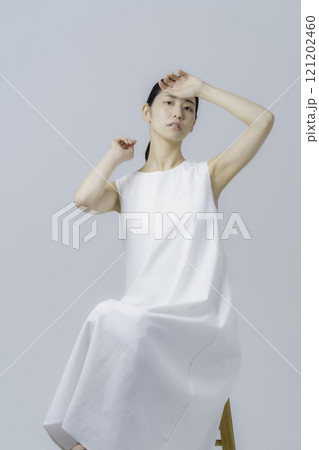 グレー背景の白いワンピースを着る若い女性のポートレート　縦位置 121202460