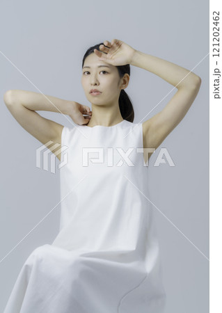 グレー背景の白いワンピースを着る若い女性のポートレート　縦位置 121202462