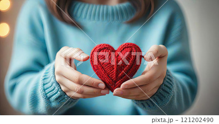 Female hands in a warm blue sweater hold a red knitted heart Female hands in a warm blue sweater hold a red knitted heart 121202490