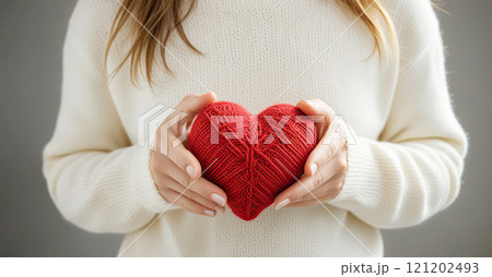 Female hands in a warm white sweater hold a red knitted heart Female hands in a warm white sweater hold a red knitted heart 121202493