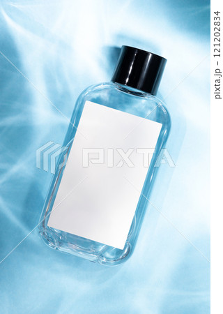 A cosmetic glass bottle with a blank white label on a pastel blue background. 121202834