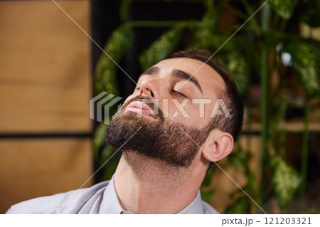 Young man dressed formal wear tilts his head back and sits with closed eyes after applying moisturizing drops. Disease and treatment. 121203321