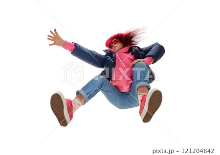 Young woman with flowing red hair wearing bright pink hoodie, blue jacket, and rolled-up jeans against white studio background. Bottom view 121204842