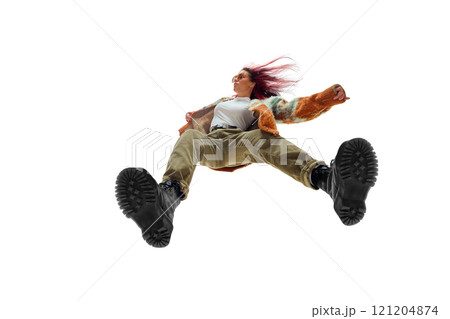 Dynamic low-angle image of confident young woman with red hair, wearing colorful jacket and stylish pants against white studio background 121204874