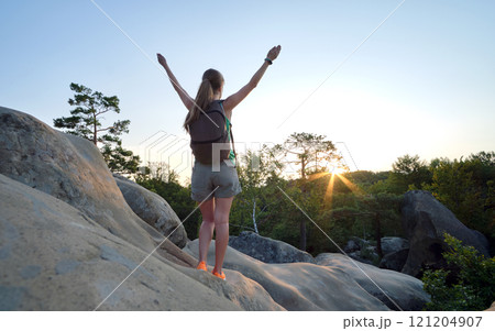 Young woman hiker standing alone with outstretched arms on mountain footpath enjoying view of morning nature on wilderness trail at sunrise. Active way of life concept 121204907