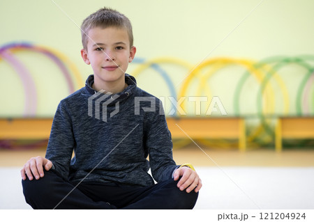 Young child boy sitting and relaxiong on the floor inside sports room in a school after training. 121204924