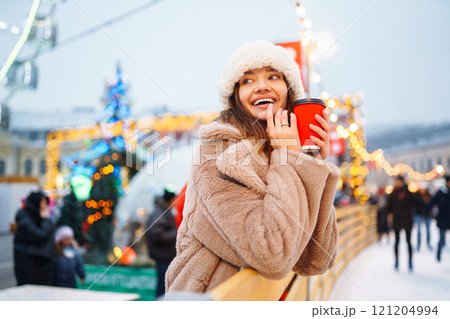 Woman with coffee in winter over outdoor ice skating rink on background. Winter holidays concept. Woman with coffee in winter over outdoor ice skating rink on background. Winter holidays concept. 121204994