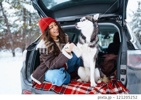 Happy woman with her husky having a picnic in the trunk of a car on a snowy road. Travel concept. Happy woman with her husky having a picnic in the trunk of a car on a snowy road. Travel concept. 121205252
