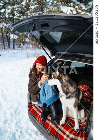 Happy woman with her husky having a picnic in the trunk of a car on a snowy road. Travel concept. Happy woman with her husky having a picnic in the trunk of a car on a snowy road. Travel concept. 121205255