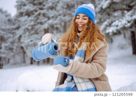 Smiling woman with a thermos in a snowy forest enjoying nature. Adventure concept. Lifestyle. Smiling woman with a thermos in a snowy forest enjoying nature. Adventure concept. Lifestyle. 121205599