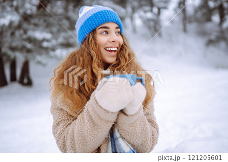Smiling woman with a thermos in a snowy forest enjoying nature. Adventure concept. Lifestyle. 121205601