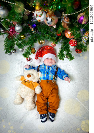 Baby Celebrating Christmas Under the Tree With a Teddy Bear and Festive Decorations 121205964