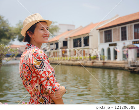 Young woman in ethnic dress and hat exploring the vibrant streets of Malacca, Malaysia. A blend of cultural heritage, colorful architecture, and tropical charm. Perfect travel and lifestyle moments. 121206389