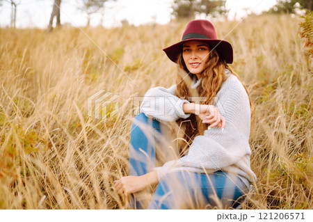 Stylish woman in sweater and hat enjoys autumn nature. People, freedom, lifestyle, travel concept. 121206571