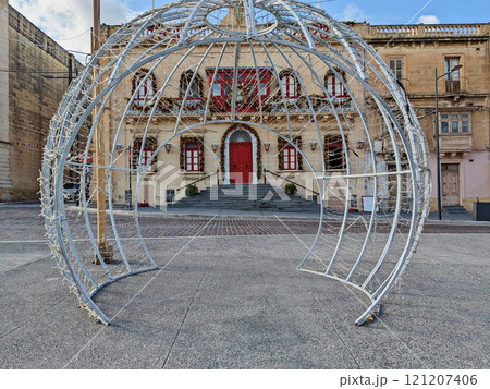 Christmas light installation opposite historic Maltese building adorned with festive wreaths and red accents, creating holiday scene Christmas light installation opposite historic Maltese building adorned with festive wreaths and red accents, creating holiday scene 121207406