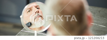 Website header shot of Reflection in small table mirror of mature man brushing neat beard during daily hair care routine at home, copy space Website header shot of Reflection in small table mirror of mature man brushing neat beard during daily hair care routine at home, copy space 121208213