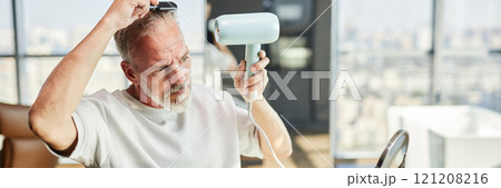 Website header shot of handsome mature man styling hair with hairdryer after taking bath during self care routine at home, copy space 121208216