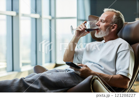 Side view of successful mature man drinking red wine while relaxing in comfy armchair indulging in delicious alcohol beverage on weekend at home, copy space Side view of successful mature man drinking red wine while relaxing in comfy armchair indulging in delicious alcohol beverage on weekend at home, copy space 121208227