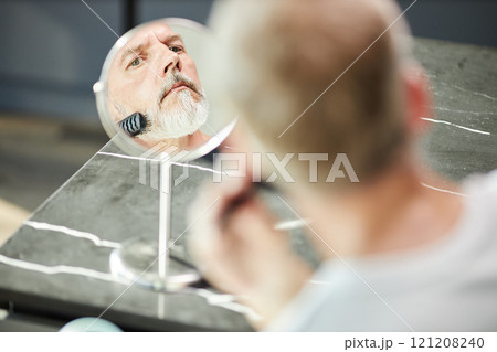 Reflection in small table mirror of mature man grooming neat beard bruising hair with hairbrush during daily self care routine at home, copy space Reflection in small table mirror of mature man grooming neat beard bruising hair with hairbrush during daily self care routine at home, copy space 121208240
