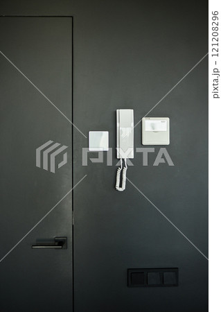 Vertical shot of intercom electronic panel and handset with microphone for talking to guests hanging on black wall inside minimalist apartment in residential building, copy space Vertical shot of intercom electronic panel and handset with microphone for talking to guests hanging on black wall inside minimalist apartment in residential building, copy space 121208296