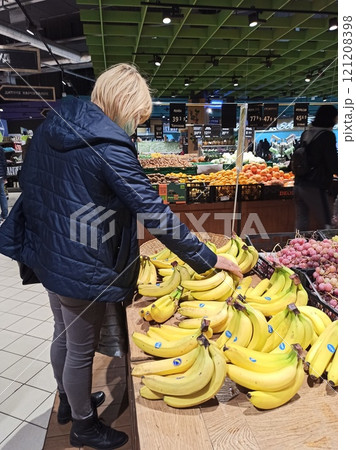 Modern woman choosing bananas in supermarket. Woman buys fruit in store 121208398