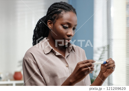 Portrait shot of serious young African American woman holding pregnancy test waiting for result in bathroom, copy space 121209620