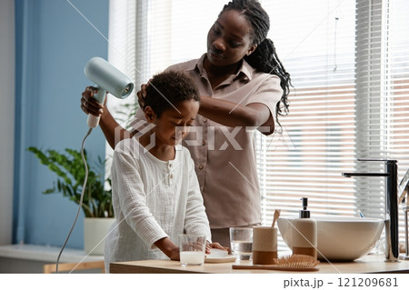 Medium shot of Black woman helping little son with drying hair in bathroom during daily hygiene routine 121209681