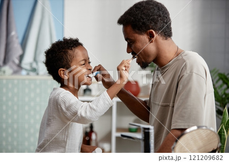 Side view of playful little Black boy and his father brushing each others teeth while having fun together in bathroom sharing happy moments 121209682