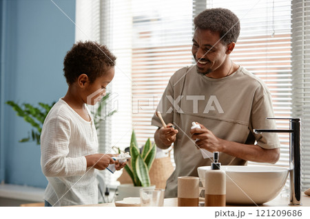 Medium shot of happy father looking at little son with affectionate smile while brushing teeth together in bathroom on Sunday morning 121209686