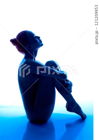 Silhouette of a woman sitting gracefully with blue lighting backdrop 121209953