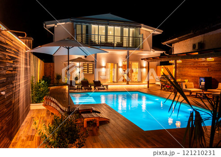 Luxury house with illuminated swimming pool and wooden deck at night. Concept of modern outdoor living space 121210231