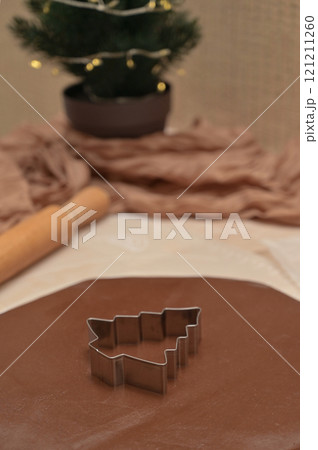 Christmas homemade baking, brown cocoa dough for baking gingerbread with tree shaped cutter, rolling pin on the table, blurred background Christmas homemade baking, brown cocoa dough for baking gingerbread with tree shaped cutter, rolling pin on the table, blurred background 121211260