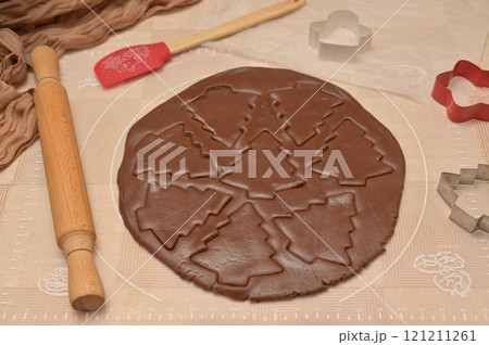 Christmas homemade baking, brown cocoa dough cut into tree shapes for baking gingerbread, cutter, rolling pin, spatula on the table Christmas homemade baking, brown cocoa dough cut into tree shapes for baking gingerbread, cutter, rolling pin, spatula on the table 121211261