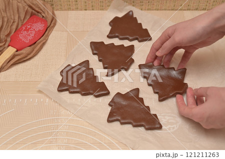 Christmas homemade baking, brown dough cut into tree shapes for baking gingerbread in a woman hands 121211263